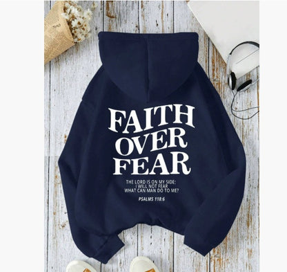 The Faith Over Fear Christian Hoodie features bold white "Faith Over Fear" text and Psalms 118:6. Styled flat with headphones, a white book, and dried flowers, this trendy unisex sweatshirt blends comfort and inspiration in an aesthetic look.