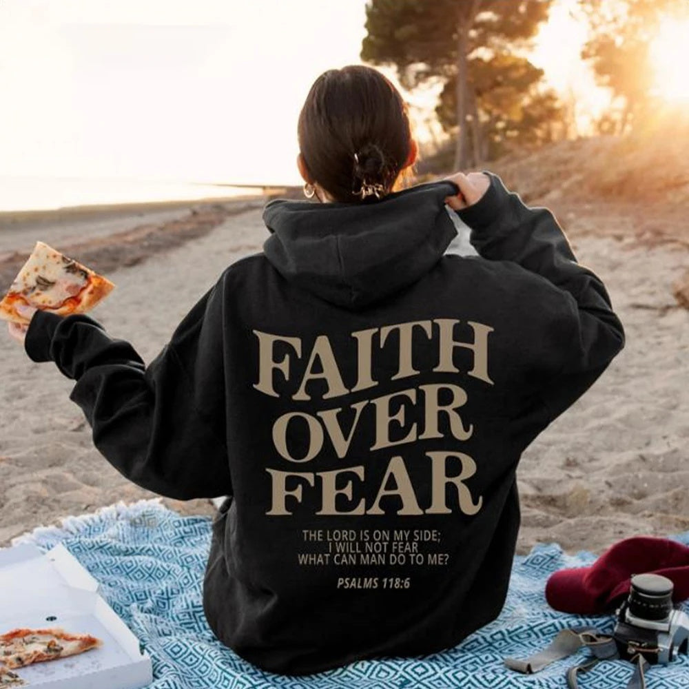 Relaxing on the beach with pizza, someone wears a Faith Over Fear Christian Hoodie featuring “THE LORD IS ON MY SIDE; I WILL NOT FEAR. WHAT CAN MAN DO TO ME? PSALMS 118:6” boldly printed on the back.