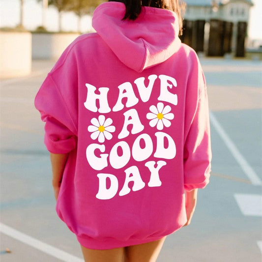 A person is outdoors wearing the Spring And Autumn Men's Women's Hoodie Flower Print Casual Hoodie in bright pink, featuring long sleeves, bold white "HAVE A GOOD DAY" text, and two daisy graphics on the back.